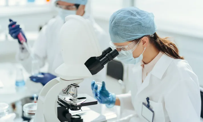 Un profesional mirando un microscopio en un laboratorio de ensayos clínicos 