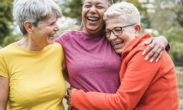 Tres mujeres de mediana edad riendo abrazadas. 